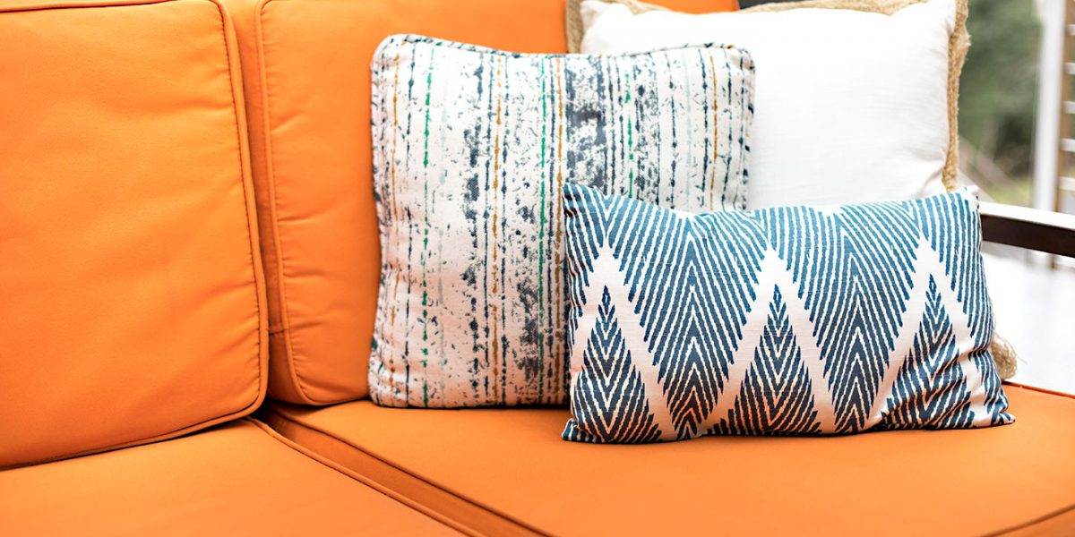 Close up on blue and white pattern throw pillows on an outdoor patio chair, with an orange couch cushion bench, on a backyard deck