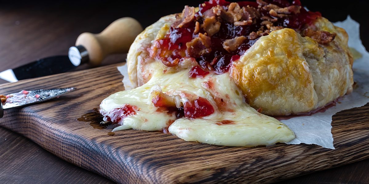 Creamy melted brie topped with cranberry sauce and bacon, pouring out of a pastry wrap