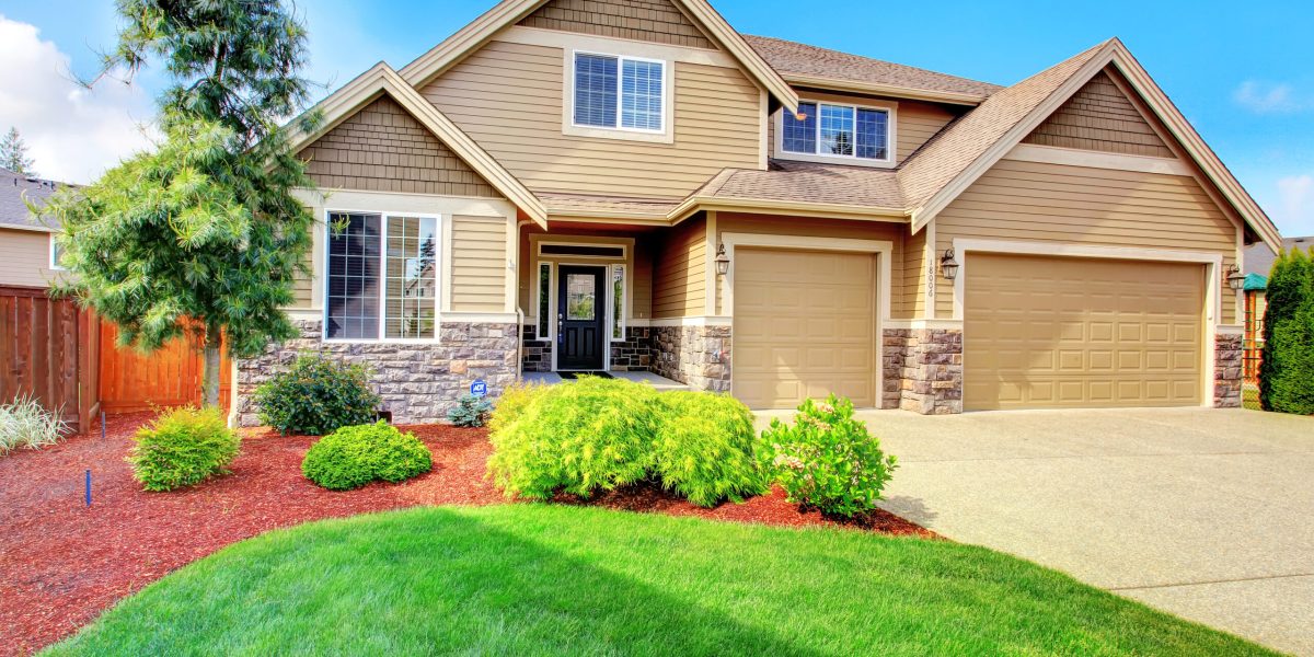 Clapboard siding house  with stone trim. View of  entrance porch, beautiful flower bed with green lawn, bushes and fir tree