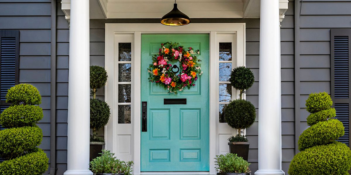 Beautifully decorated front door of traditional home. Brick path and trimmed hedges.