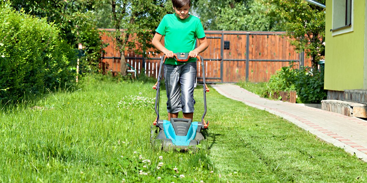 Boy cutting grass around the house in summertime - focusing on the operation