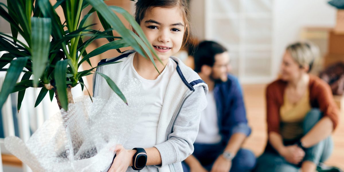 Portrait of happy girl carrying potted plant while relocating in a new home with her parents.